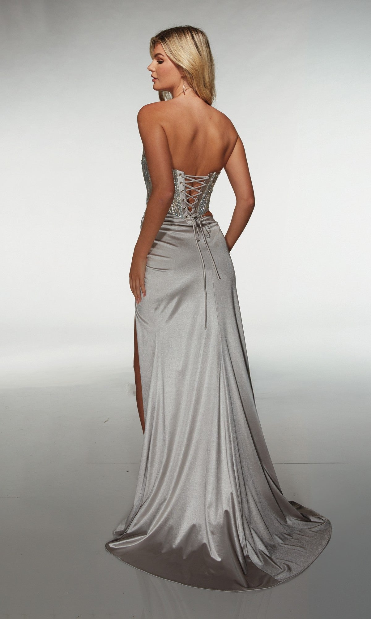A woman faces away in the Alyce 62087 long prom dress, featuring silver satin, a sweetheart neckline, beaded corset details, lace-up back, and a sweeping floor-length train.